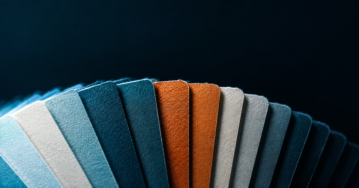 Macro of a fanned colour swatch deck under raking teal light with two identical amber blades sitting side by side